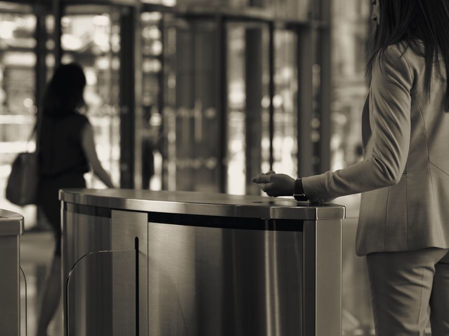 A visitor presenting a credential at a lobby speedgate while a second person passes through behind her.
